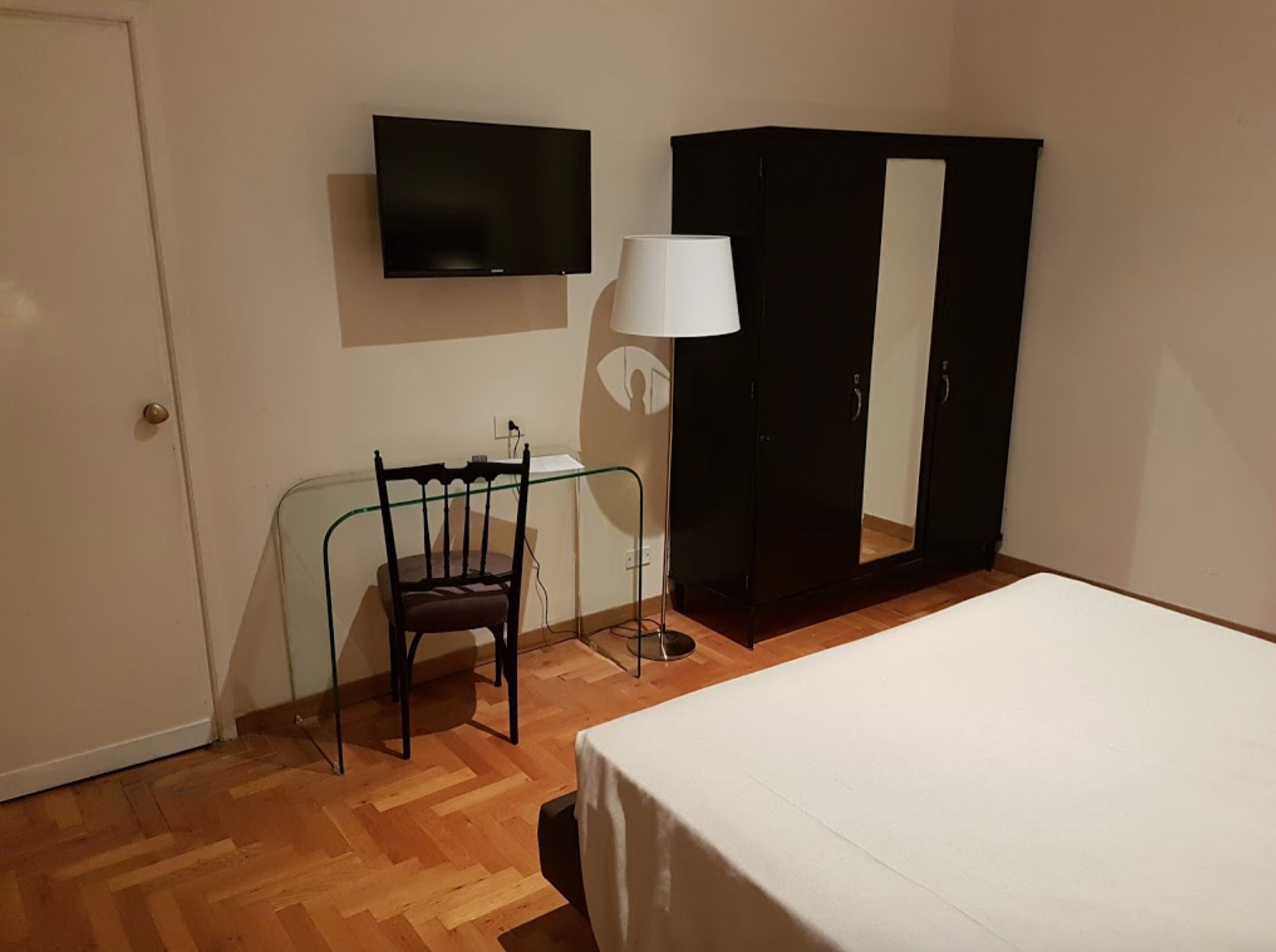 A room with a bed, a chair, a desk, a TV, and a wardrobe.