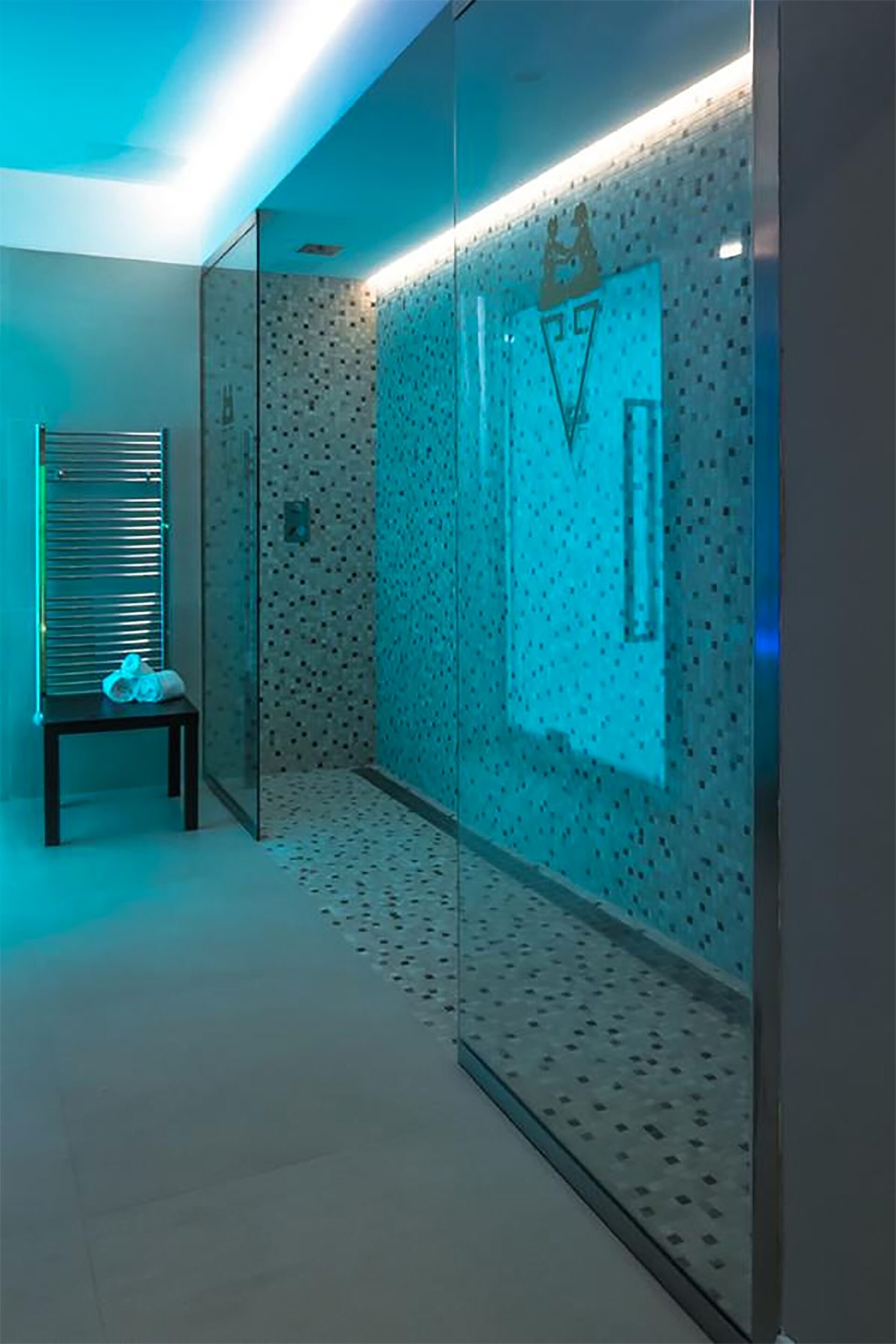 A modern bathroom with a glass shower enclosure, a bench, and a wall-mounted towel rack.