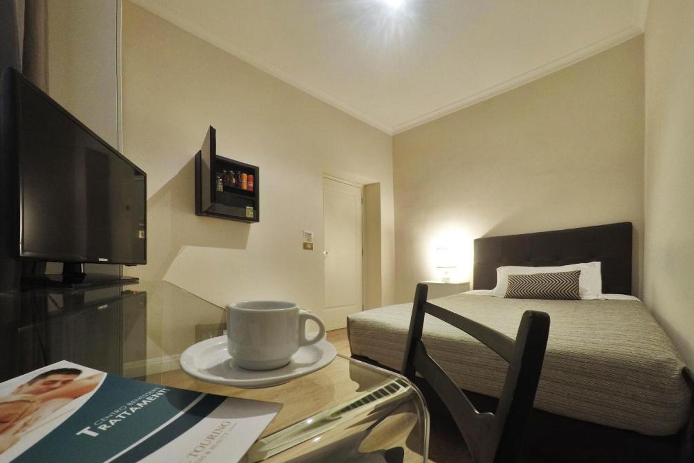 Una habitación de hotel con una cama, televisión, una taza sobre una mesa y una puerta.