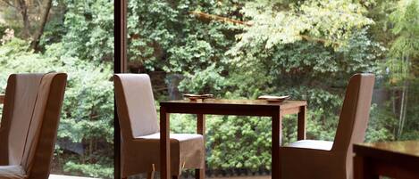 A dining area with a table and chairs, a view of a forest through large windows.