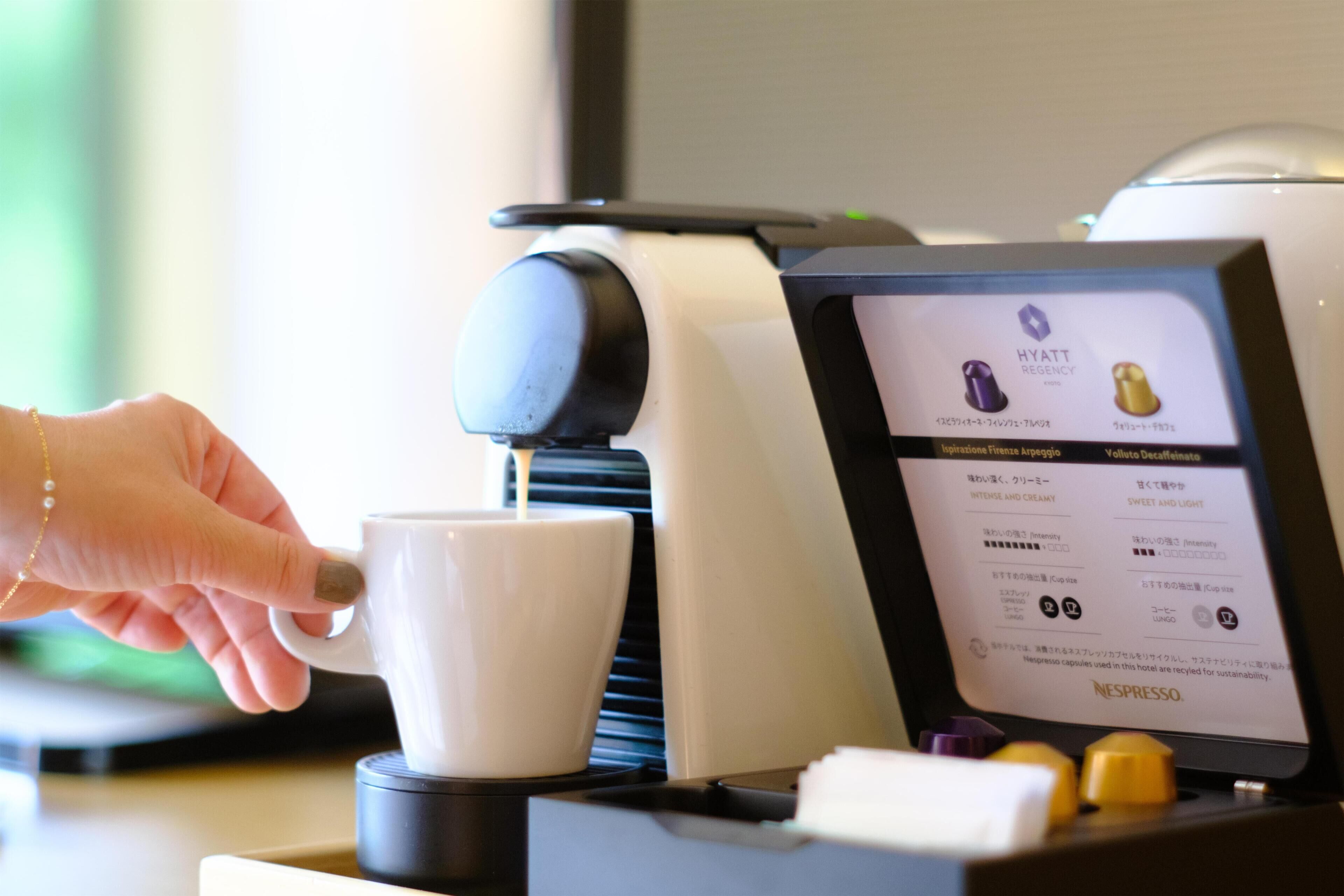 A hand pressing a button on a coffee machine, with a digital display indicating options for espresso and decaffeinated coffee.
