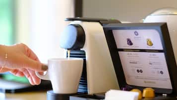 A hand pressing a button on a coffee machine, with a digital display indicating options for espresso and decaffeinated coffee.