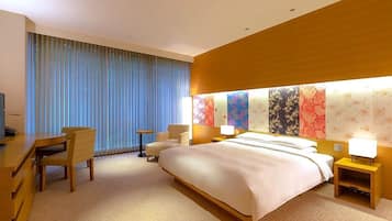 Habitación de hotel con una cama grande, un escritorio, dos sillas, un televisor y una pared con motivos florales de colores.