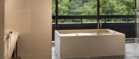 Une salle de bain avec une baignoire, un banc et une grande fenêtre donnant sur les arbres.