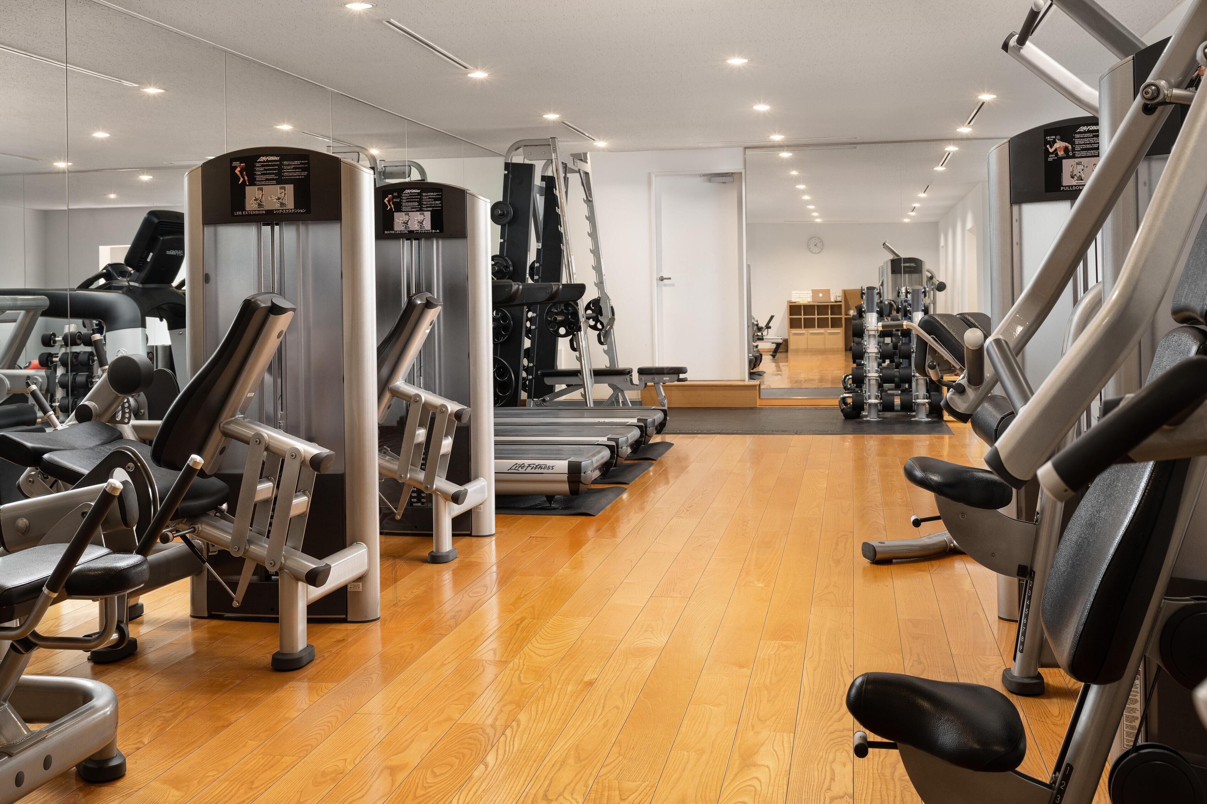 A gym with various exercise machines, a treadmill, and a mirrored wall.