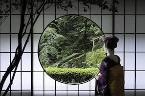A traditional Japanese room with tatami flooring, a shoji screen, and a view of a lush garden through a circular window. - Hyatt Regency Kyoto (Kyoto)
