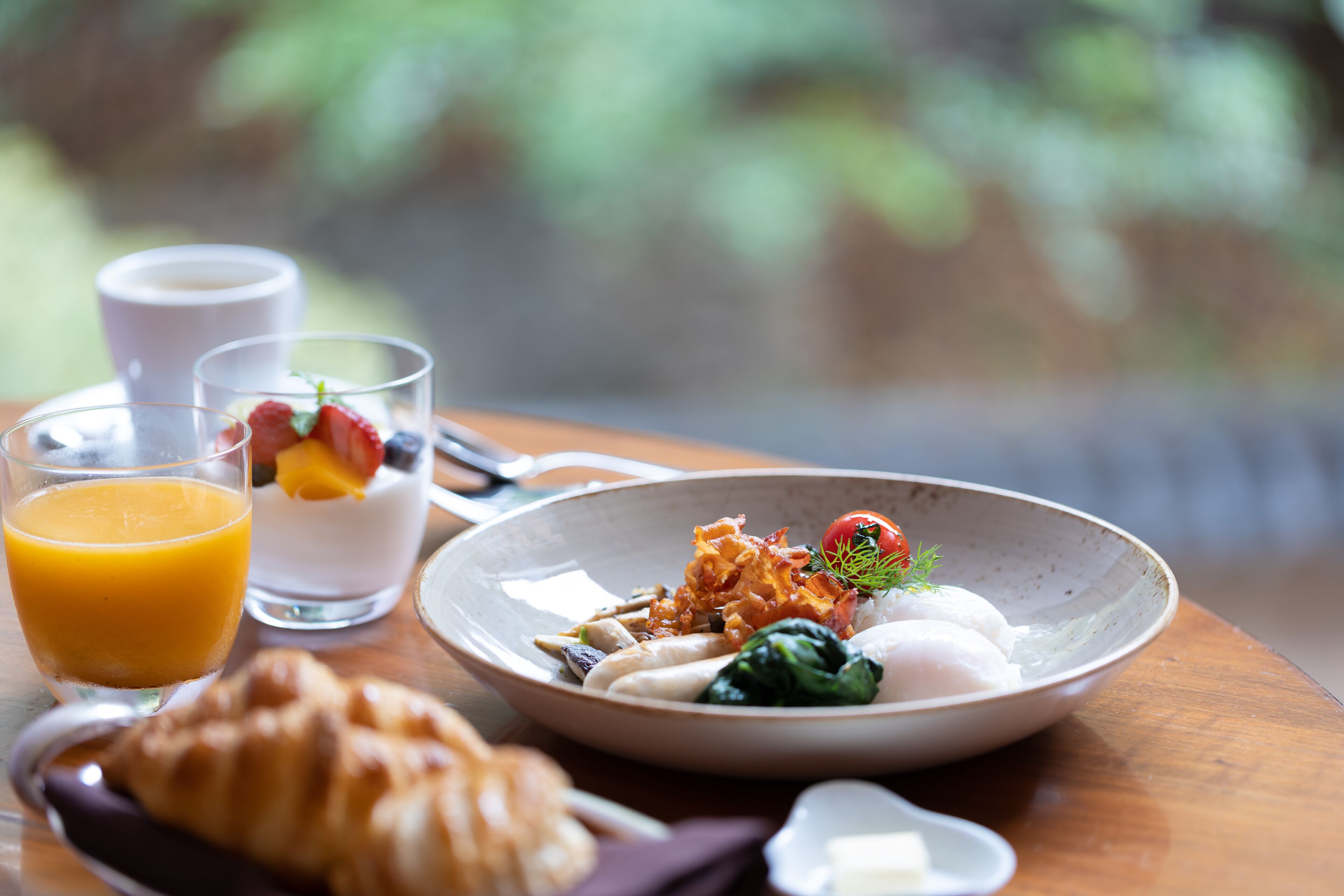 A breakfast setting with a croissant, a bowl of food, and two glasses of orange juice on a wooden table.