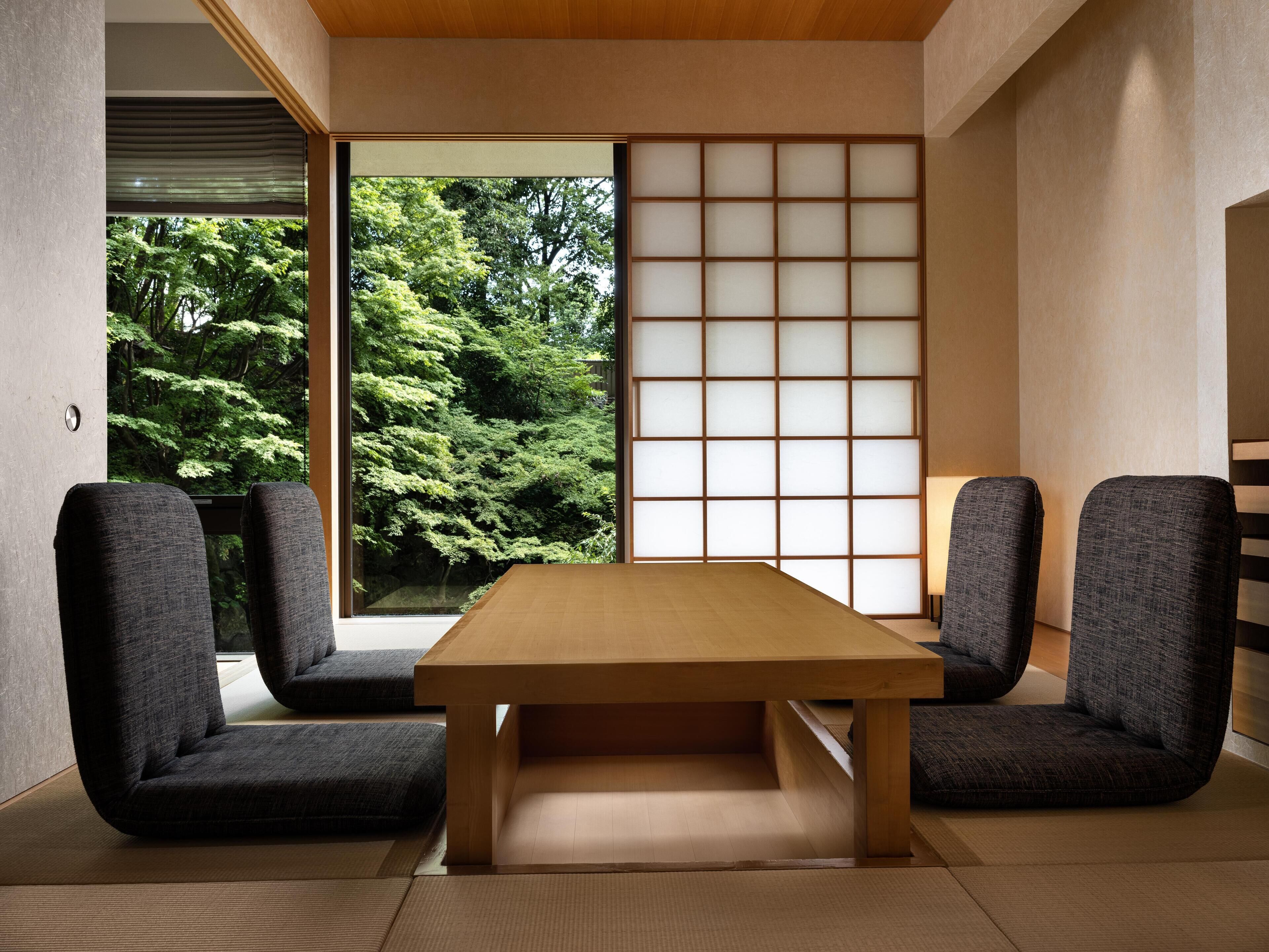 A traditional Japanese room with tatami flooring, a low wooden table, and two dark chairs.