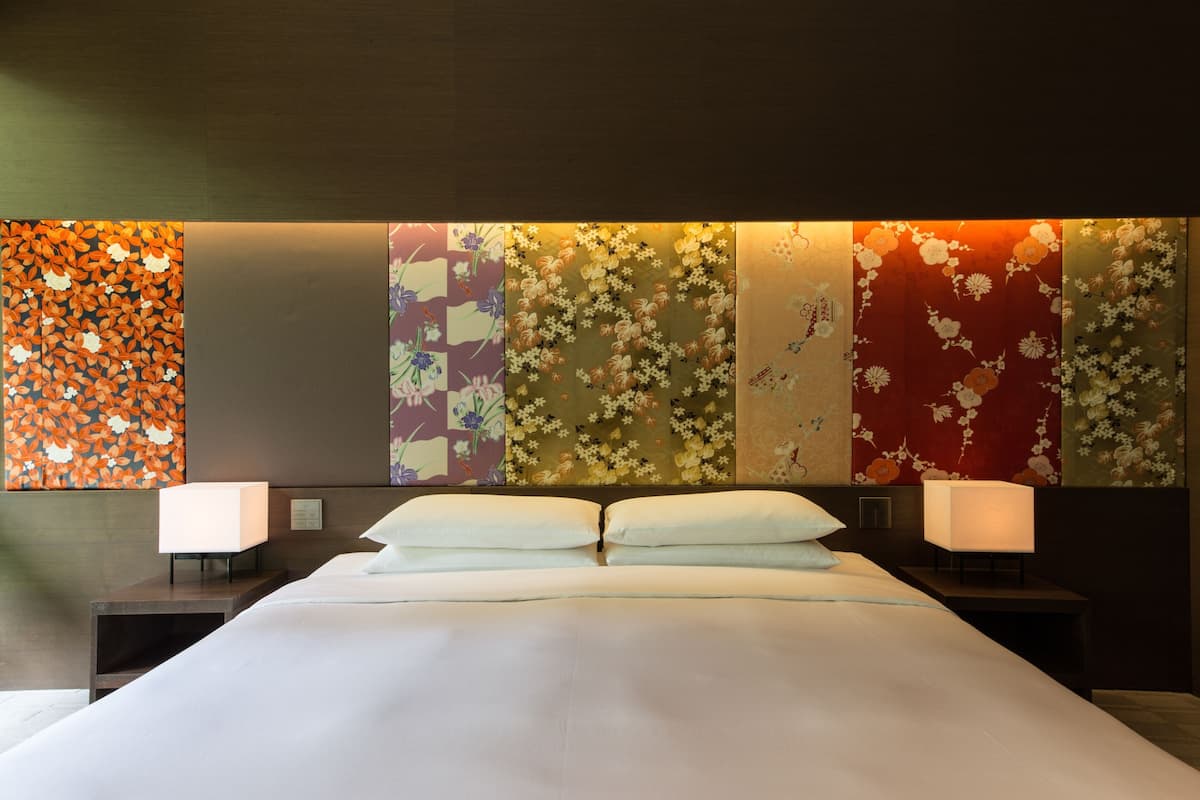 A hotel room with a large bed, two bedside tables, and a wall with floral and abstract patterns.