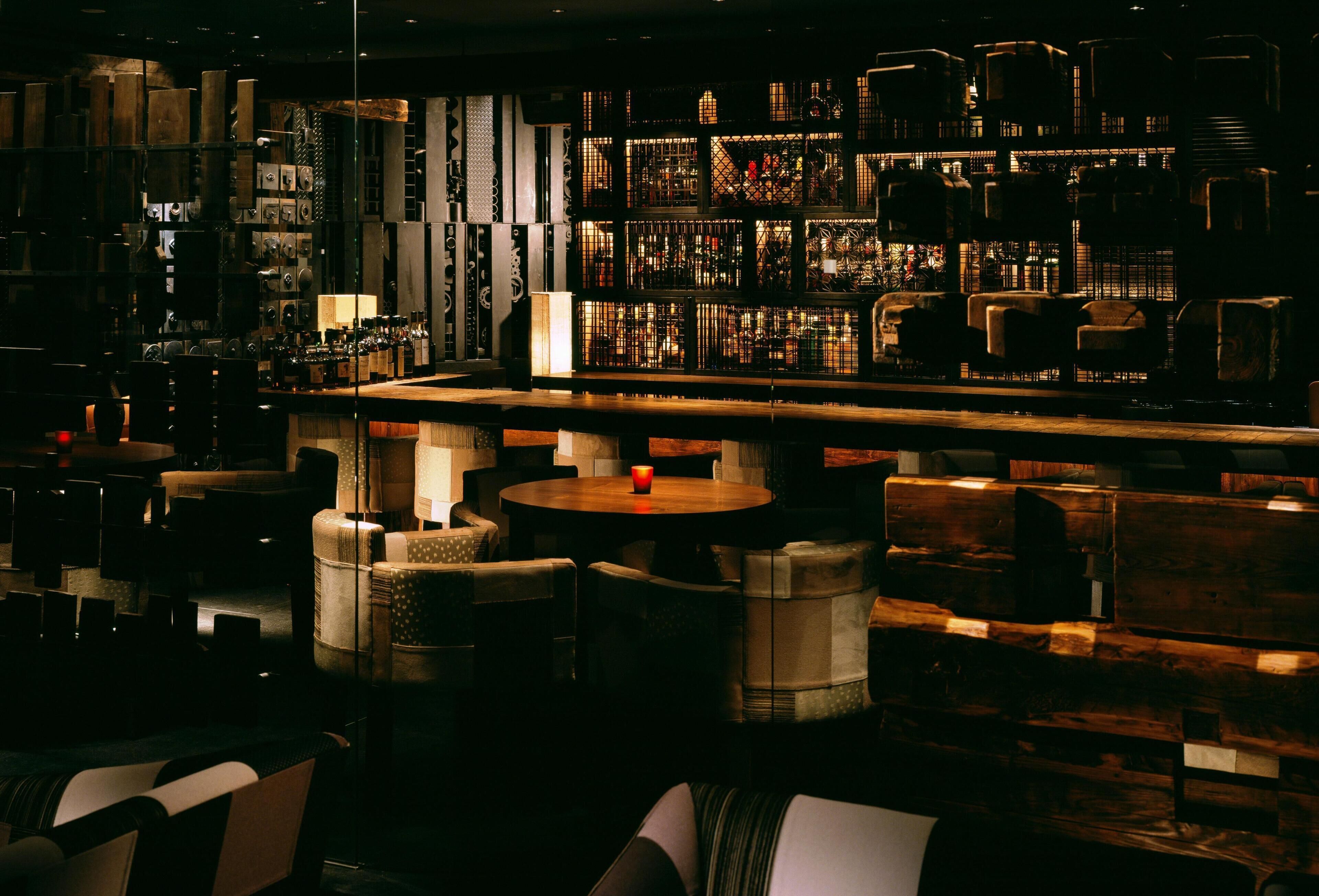 A dimly lit bar area with wooden furniture and a variety of bottles.