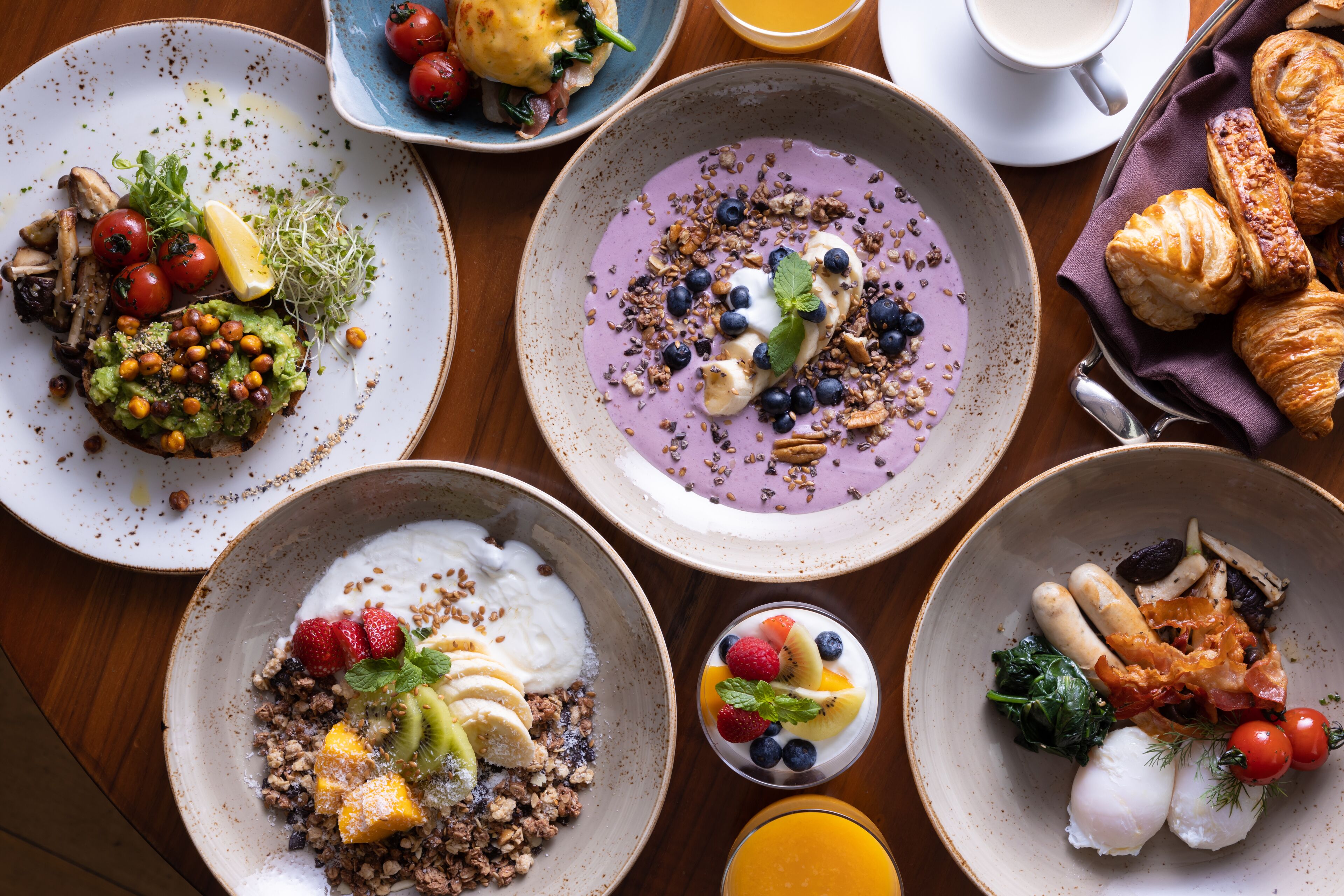 Diverse ontbijtgerechten op borden, zoals fruit, yoghurt en gebak.