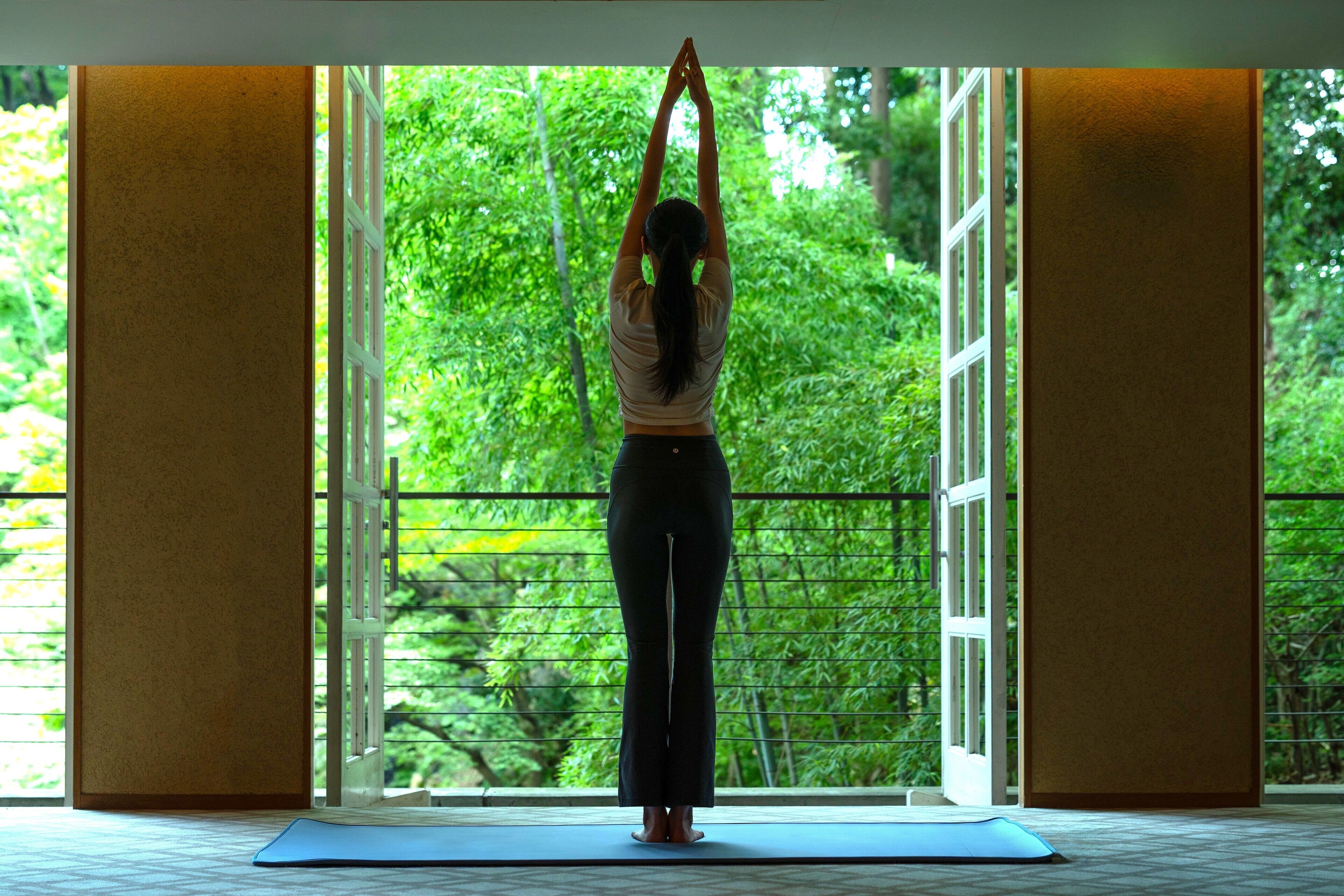 Una persona realiza una postura de yoga en una habitación con amplias ventanas y vistas a la vegetación exterior.