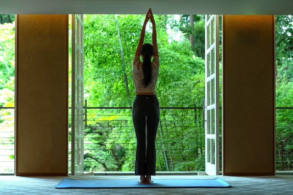 A person performing a yoga pose in a room with large windows and a view of greenery outside. - Hyatt Regency Kyoto (Kyoto)