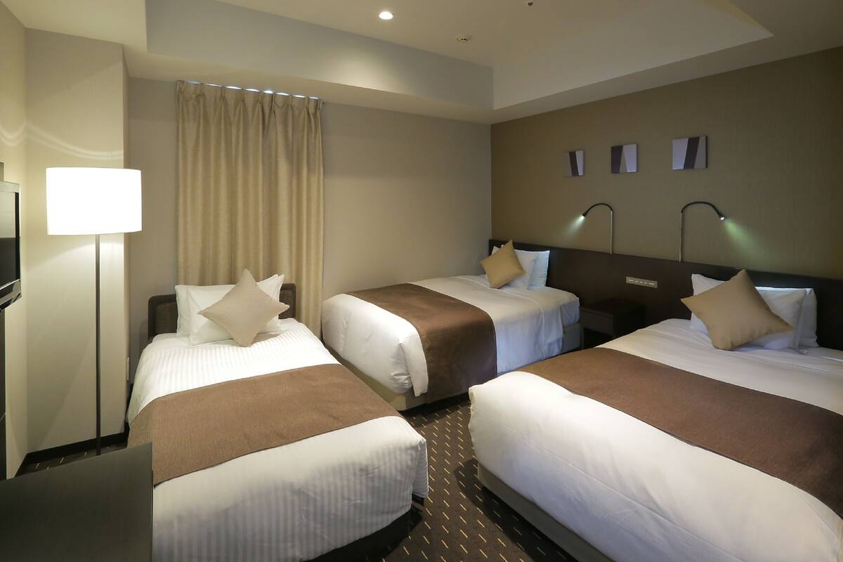 A hotel room with three beds, a TV, a lamp, and a curtain.