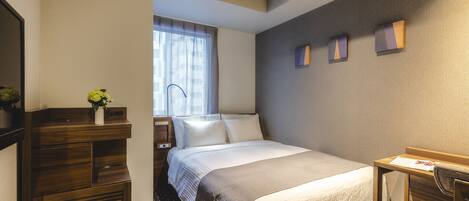 A hotel room with a bed, bedside table, chair, desk, and a window with curtains.