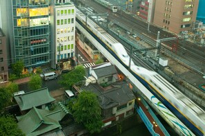 Un train à grande vitesse traverse un pont dans un quartier urbain, où se côtoient des bâtiments traditionnels et une architecture moderne.