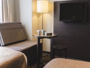A hotel room with a sofa, a small table with two cups and a book, a floor lamp, and a TV mounted on the wall. - Akihabara Washington Hotel (Tokyo)
