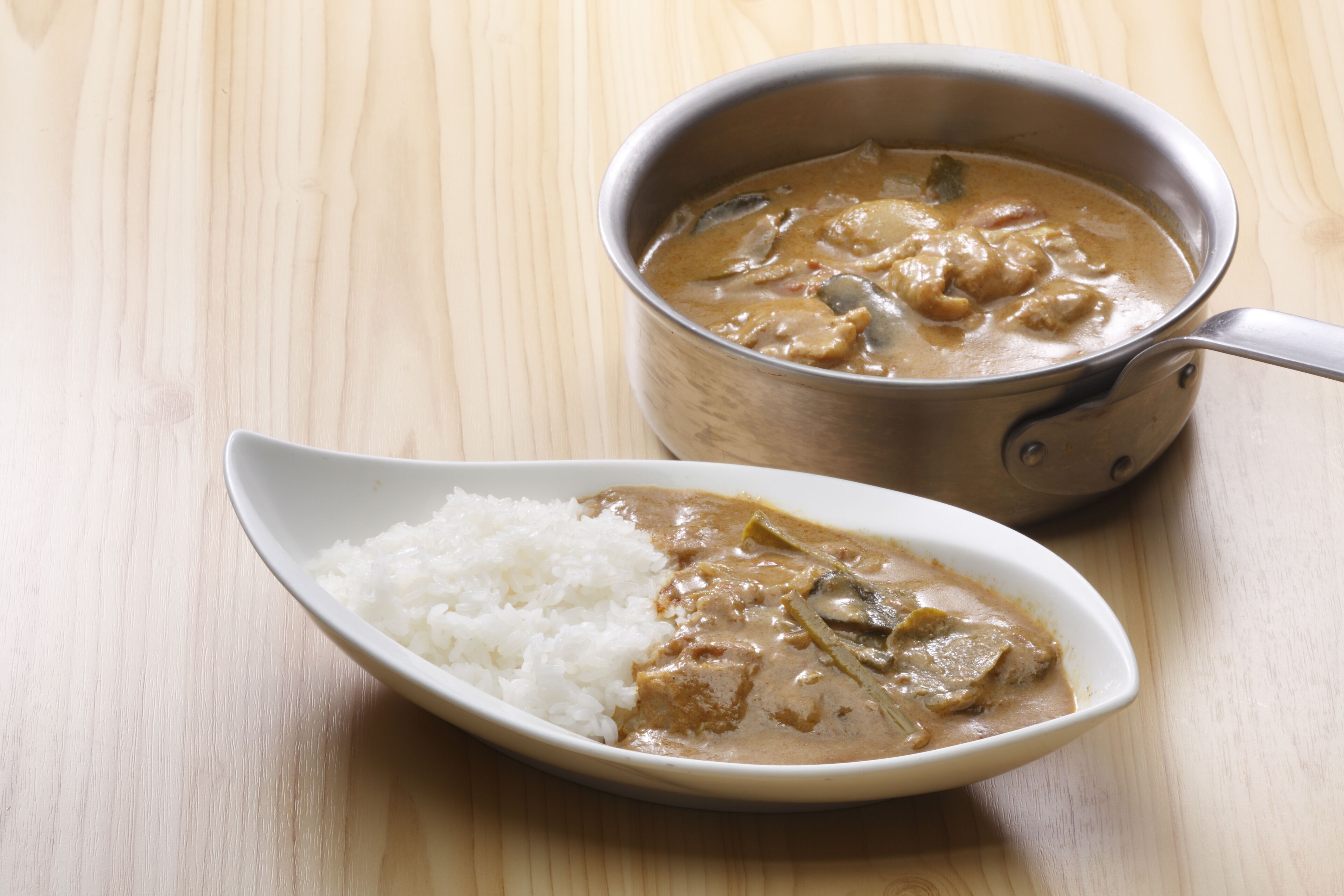 A bowl of curry with rice on a wooden table.