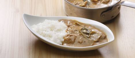 A bowl of curry with rice on a wooden table.