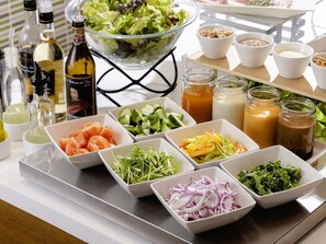 Une table garnie de divers aliments et condiments, notamment des salades, des légumes coupés en tranches et des pots de sauces.