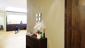 Un área de recepción con suelo de madera, un mostrador de recepción, un letrero en la pared y un jarrón decorativo con flores.