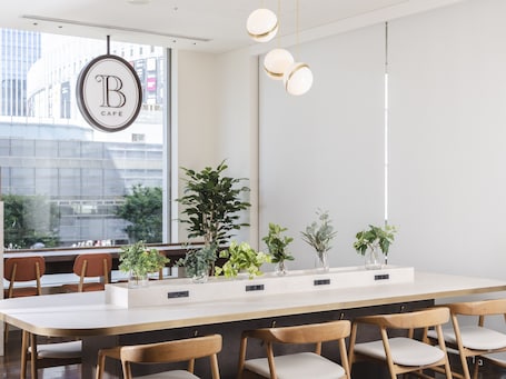 A modern cafe interior with a long counter, wooden chairs, and potted plants.