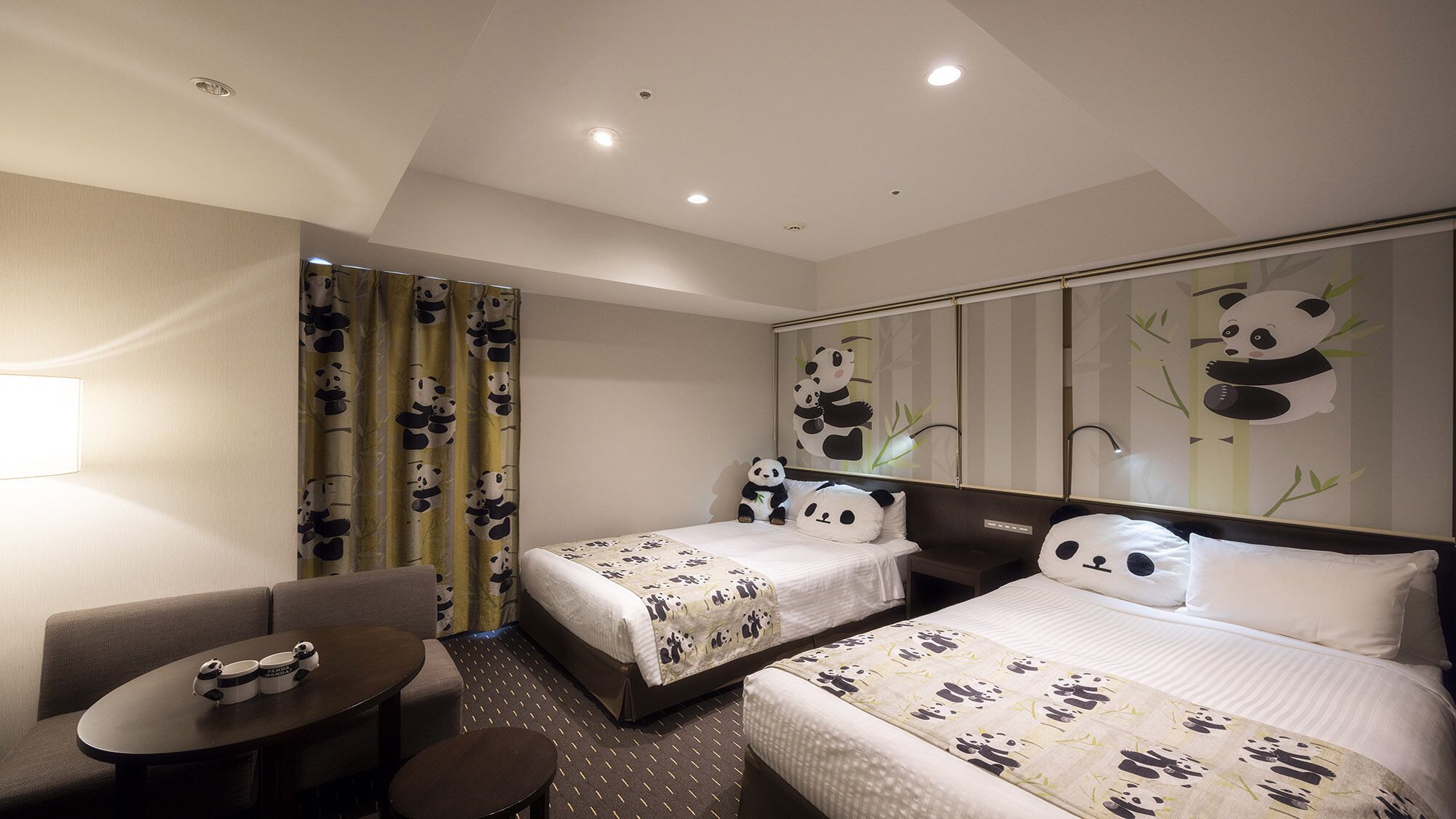 A hotel room with two beds, a sofa, a small table, and panda-themed decor.