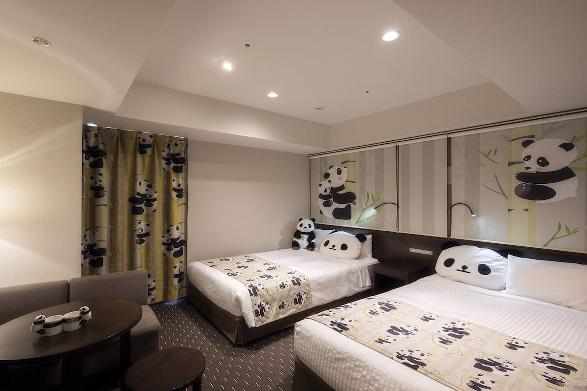 A hotel room with two beds, a sofa, a small table, and panda-themed decor.