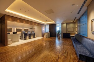 A hotel lobby with a reception desk, self-service kiosks, a seating area, and a wooden floor.