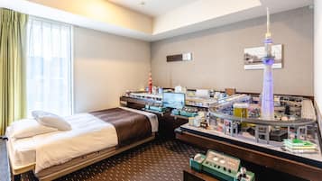 A hotel room with a bed, a desk with a model train set, and a model of a tower.