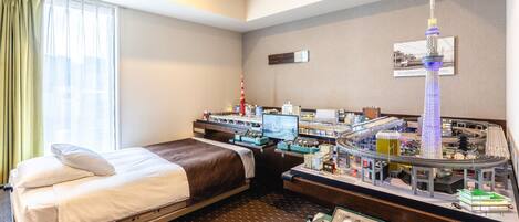 Una habitación de hotel con una cama, un escritorio con un tren de juguete y una maqueta de una torre.
