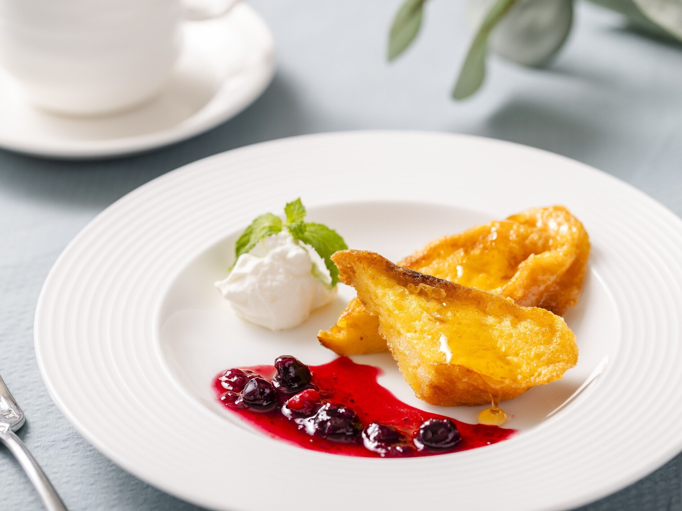A white plate with a dessert consisting of a golden-brown pastry, a dollop of cream, and a berry sauce.