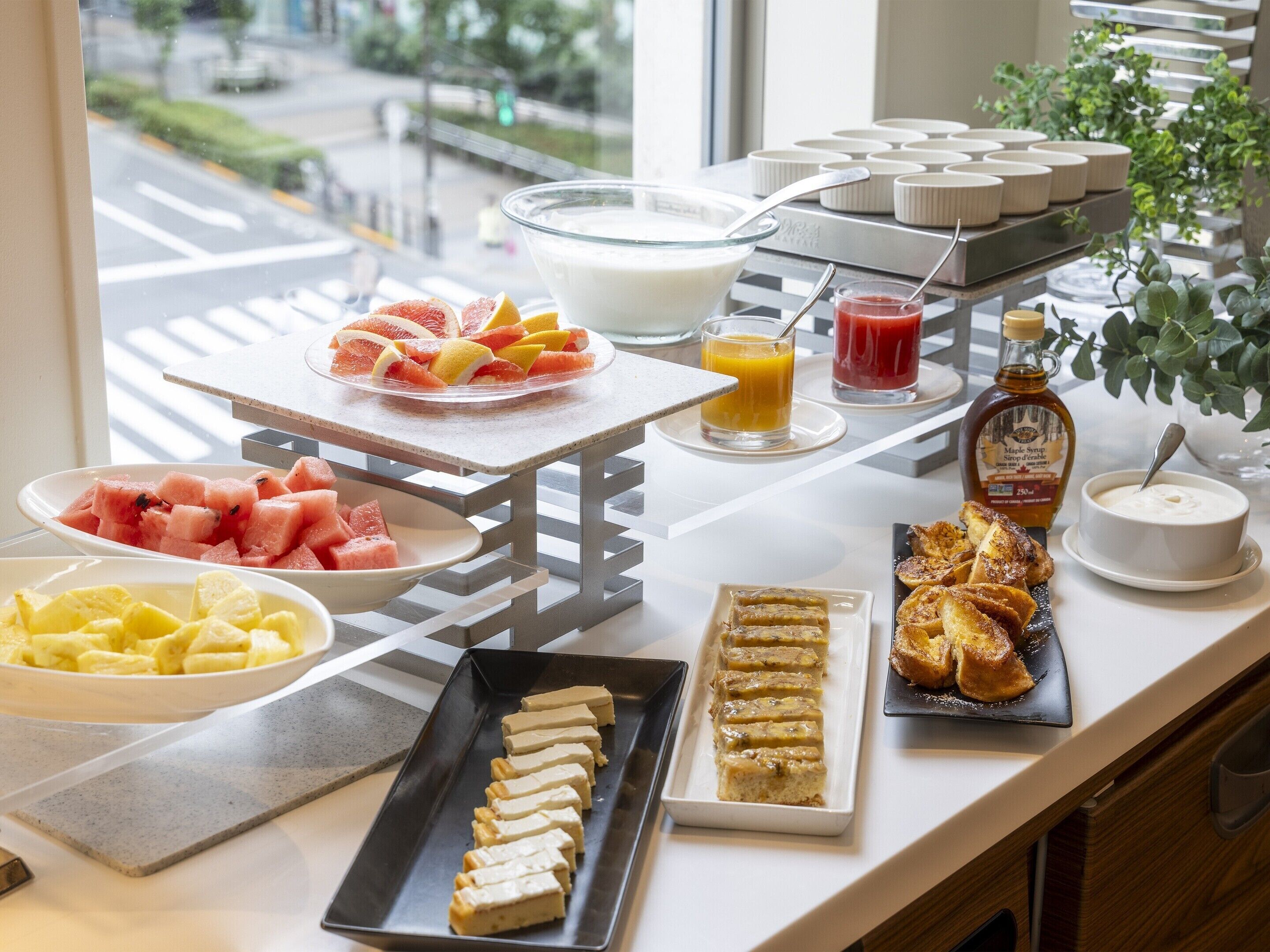 A breakfast buffet with various fruits, juices, maple syrup, and pastries.