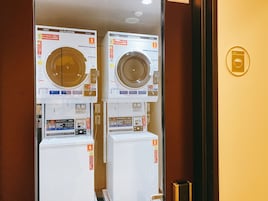 Two stacked coin-operated washing machines in a room with wooden walls and a gold-colored door.