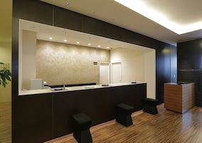 A modern reception area with a large mirror, a reception desk, and two black stools.
