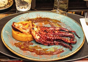 Un plato con pulpo y un pan sobre una mesa.