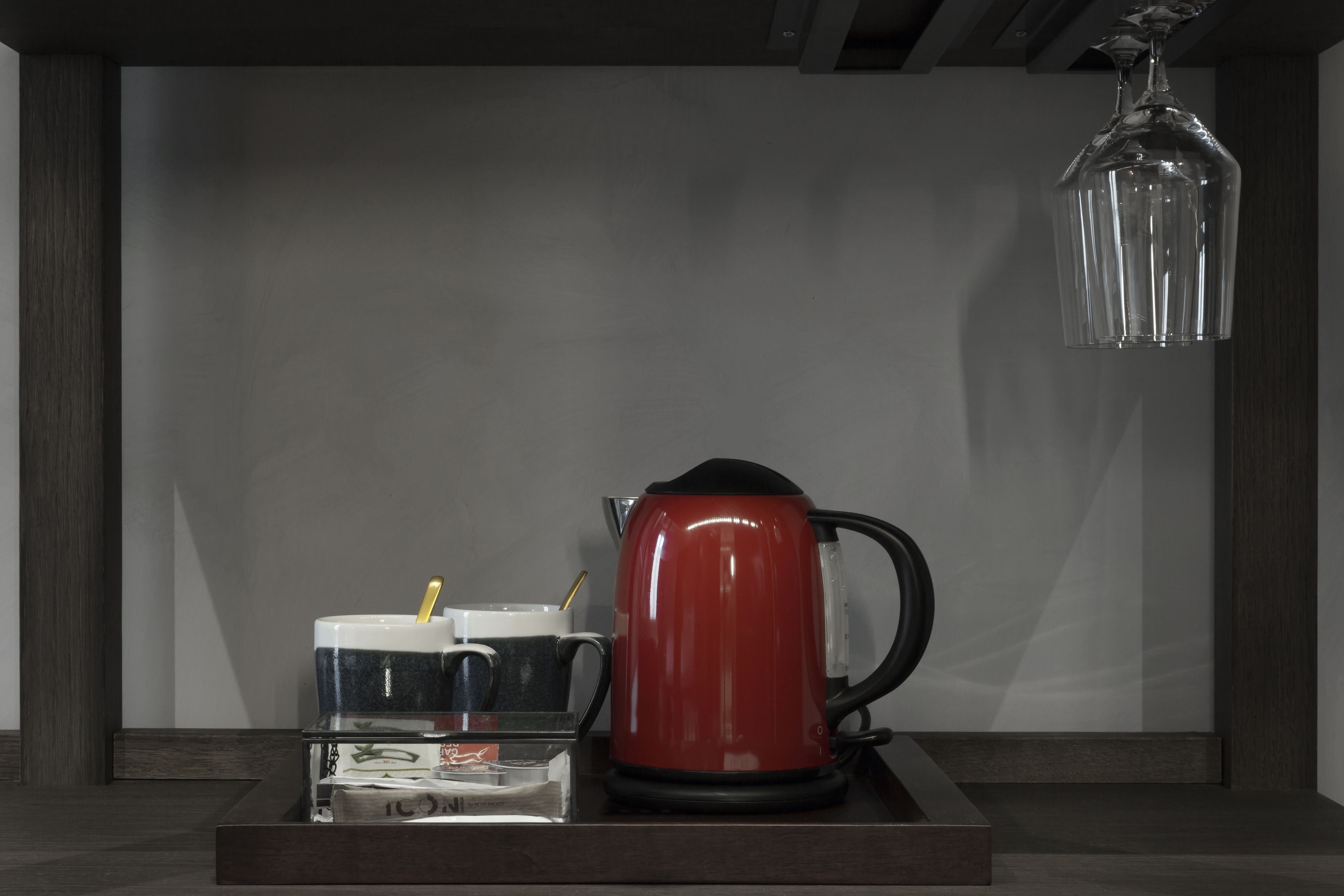 Ett modernt kök med en röd vattenkokare på ett träbricka, en kaffekanna i glas och en genomskinlig behållare i glas med en sked.