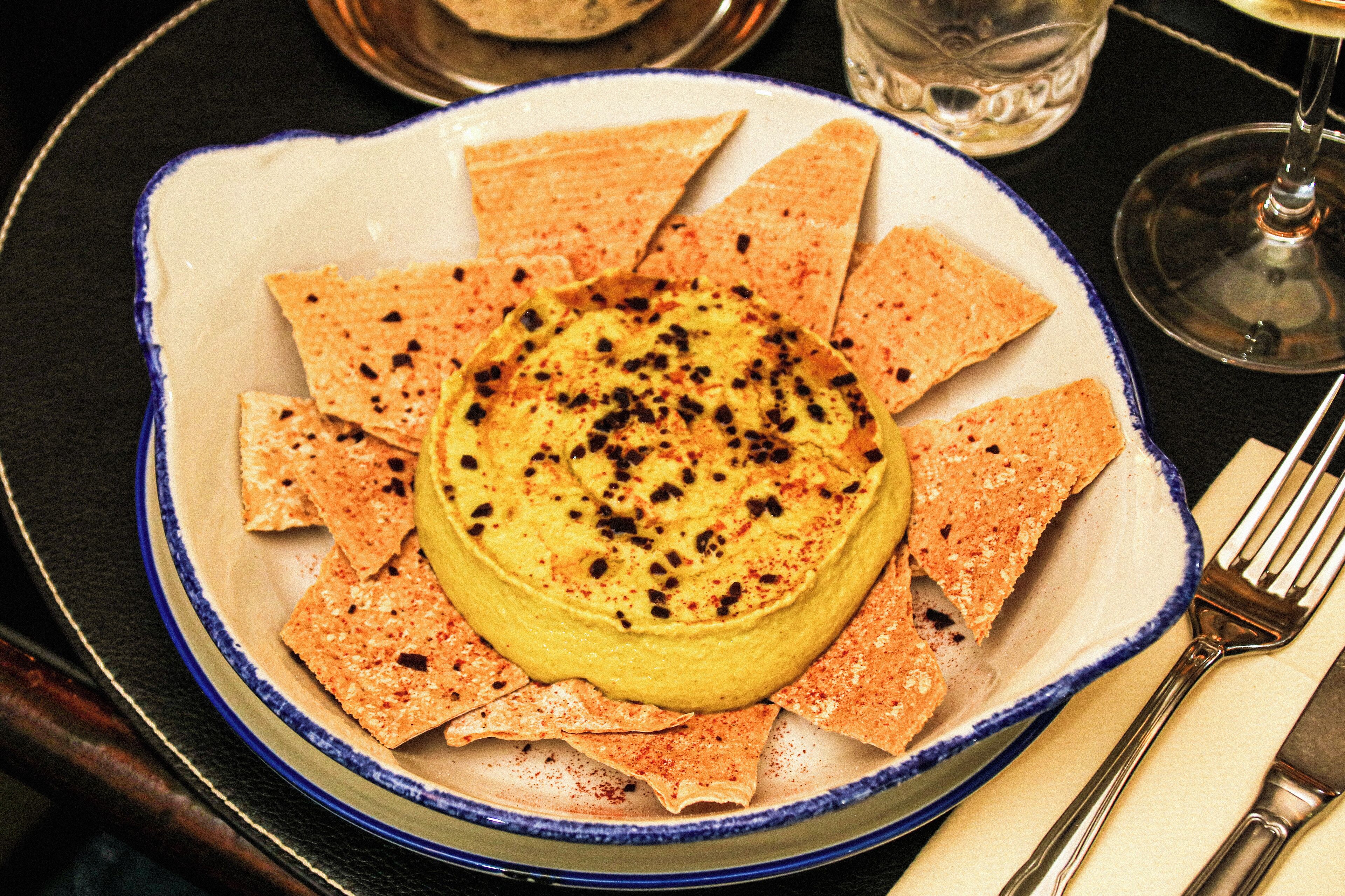 A plate of hummus with pita chips on a table.