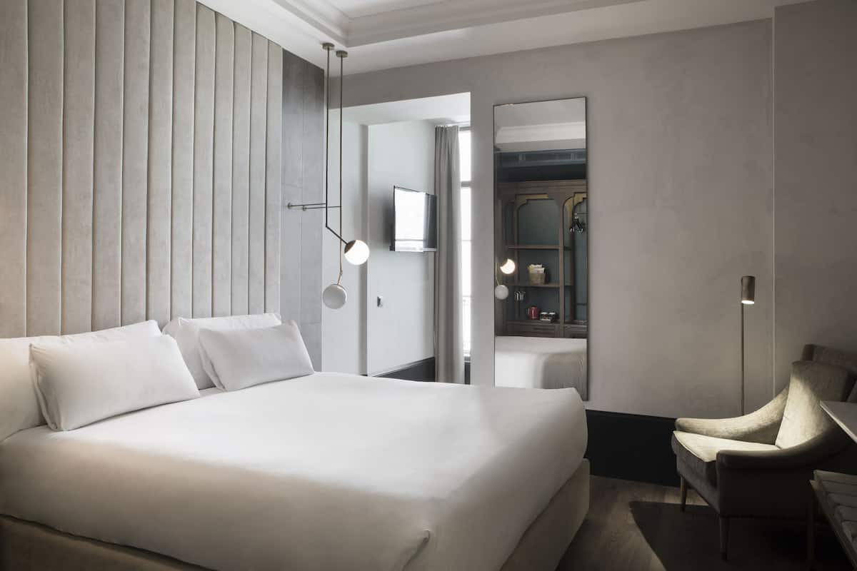 A modern hotel room with a large bed, a chair, a TV, and a mirror.