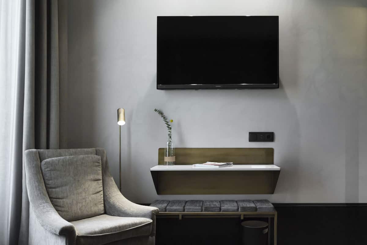 A modern room with a grey armchair, a bench, a small table with a lamp, and a mounted TV.