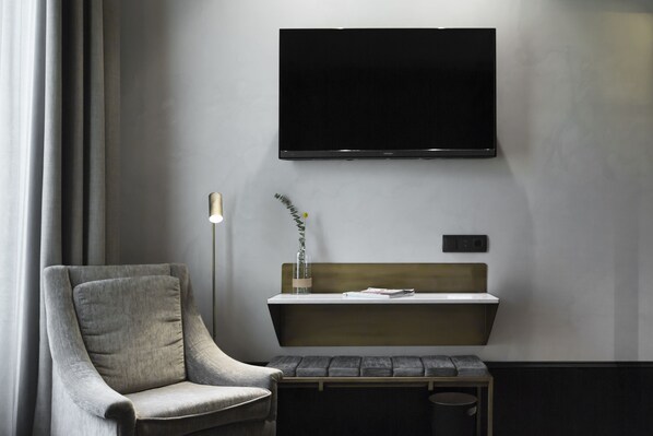 Una habitación moderna con un sillón gris, una mesita con un florero con plantas, y un televisor montado en la pared.