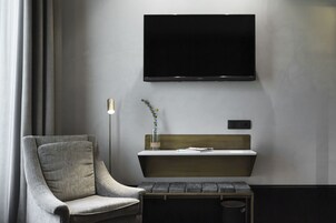 Ein modernes Zimmer mit einem grauen Sessel, einem kleinen Tisch mit Grünpflanzen und einem an der Wand befestigten Fernseher.