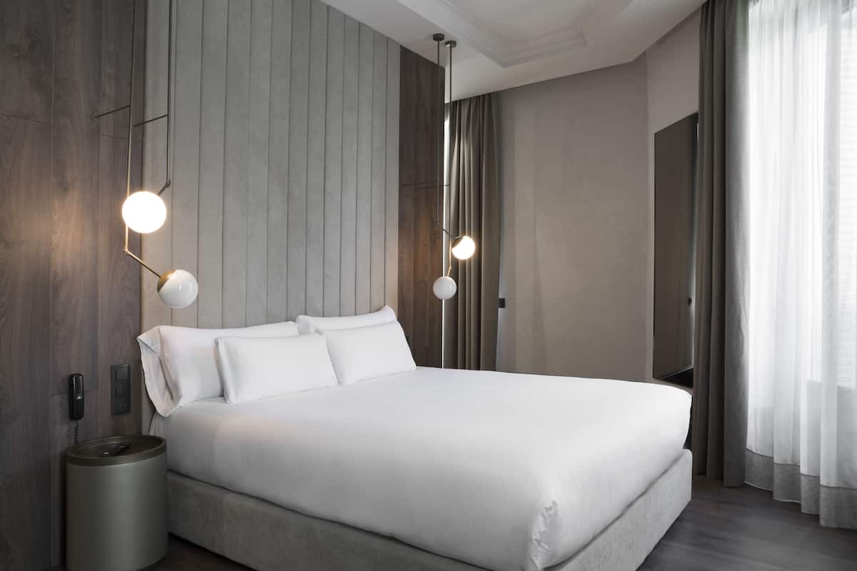A modern hotel room with a large bed, a bedside table, a lamp, and a phone.