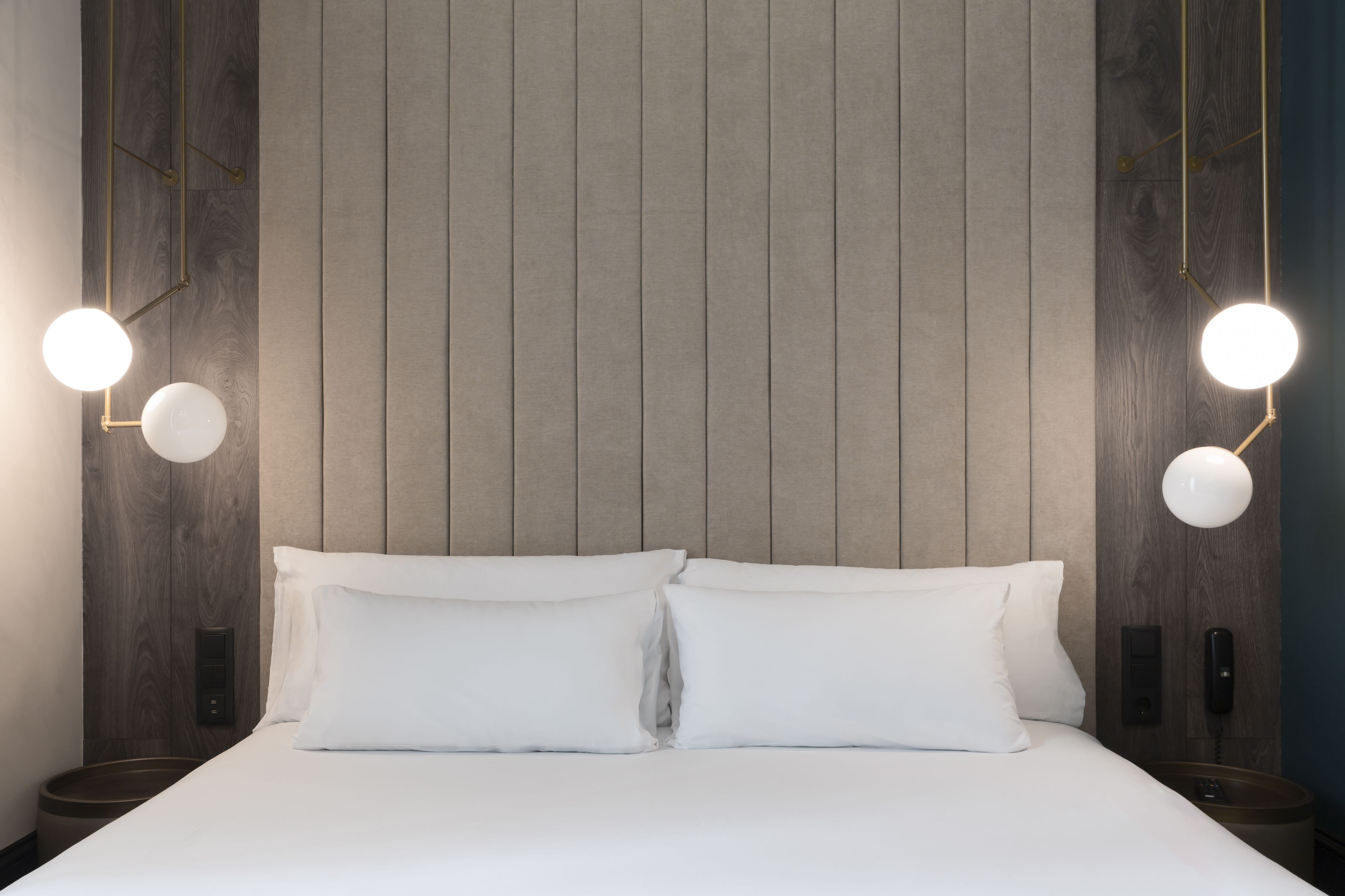 A neatly made bed with two pillows, a wall-mounted phone, and two bedside lamps.
