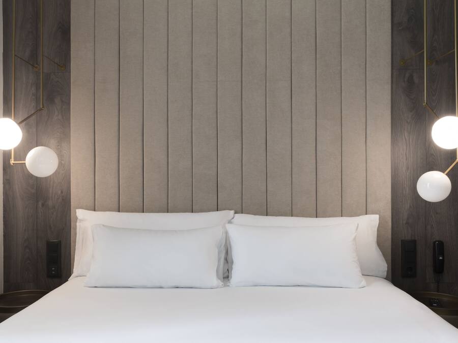 A neatly made bed with two pillows, a wall-mounted phone, and two bedside lamps.