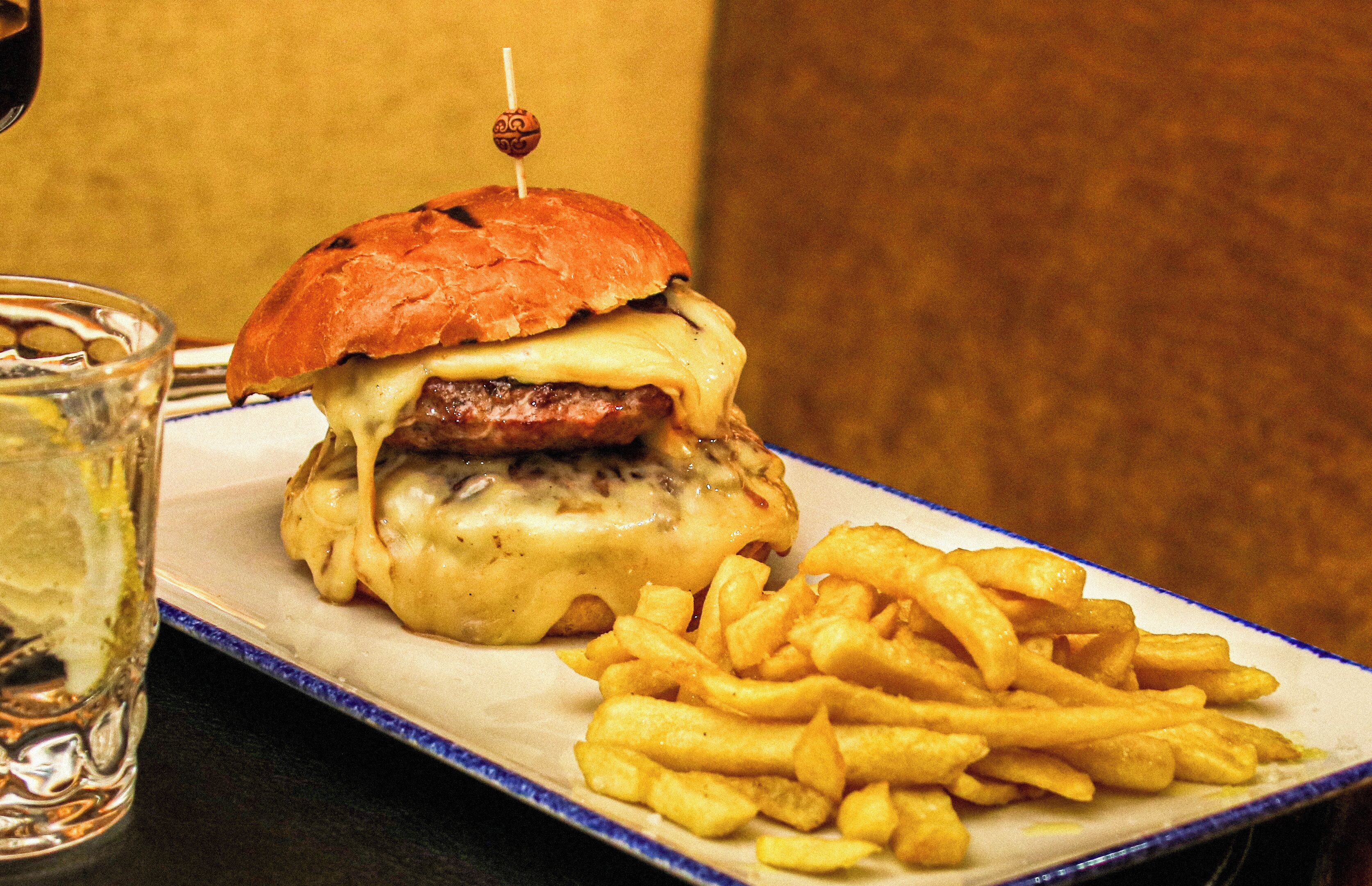 A burger with a toothpick on top, served with French fries on a white plate with a blue rim.