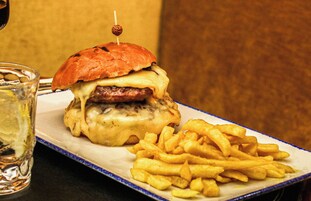 A burger with a toothpick on top, served with French fries on a white plate with a blue rim.