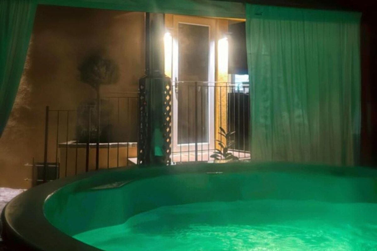 A circular hot tub with a greenish hue, surrounded by a tent-like structure with a door leading outside.