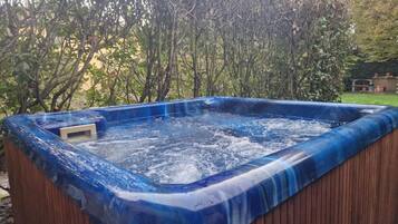 Un bain à remous avec une structure extérieure en bois et un intérieur bleu, entouré d’une végétation luxuriante.