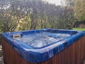 A hot tub with a wooden exterior and a blue interior, surrounded by dense foliage.